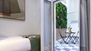 Quarto moderno com uma cama, um cobertor verde e vista para área externa com mesa e cadeiras.