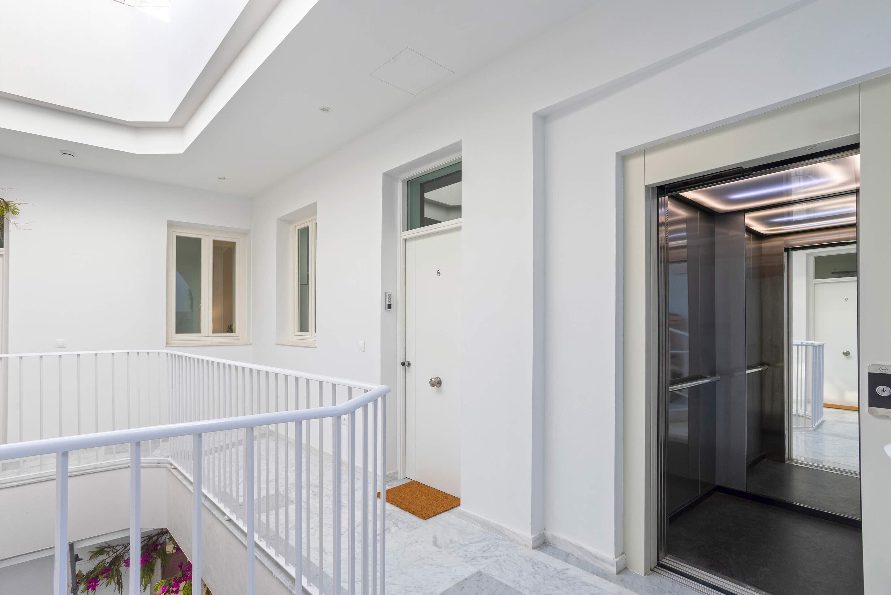 Een modern interieur met een witte balustrade, een deur naar een lift en een klein raam.