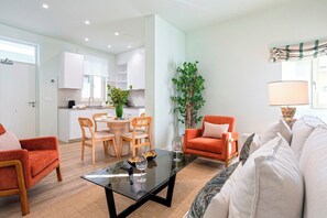 Una sala de estar moderna con una mesa de centro de vidrio, un sofá y un comedor con sillas de madera y una mesa pequeña.