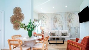 Un salon moderne avec une table de salle à manger ronde, des chaises en bois, un canapé et un téléviseur fixé au mur.