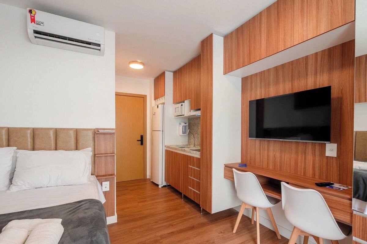 A compact hotel room with a bed, a desk, a TV, and a kitchenette.