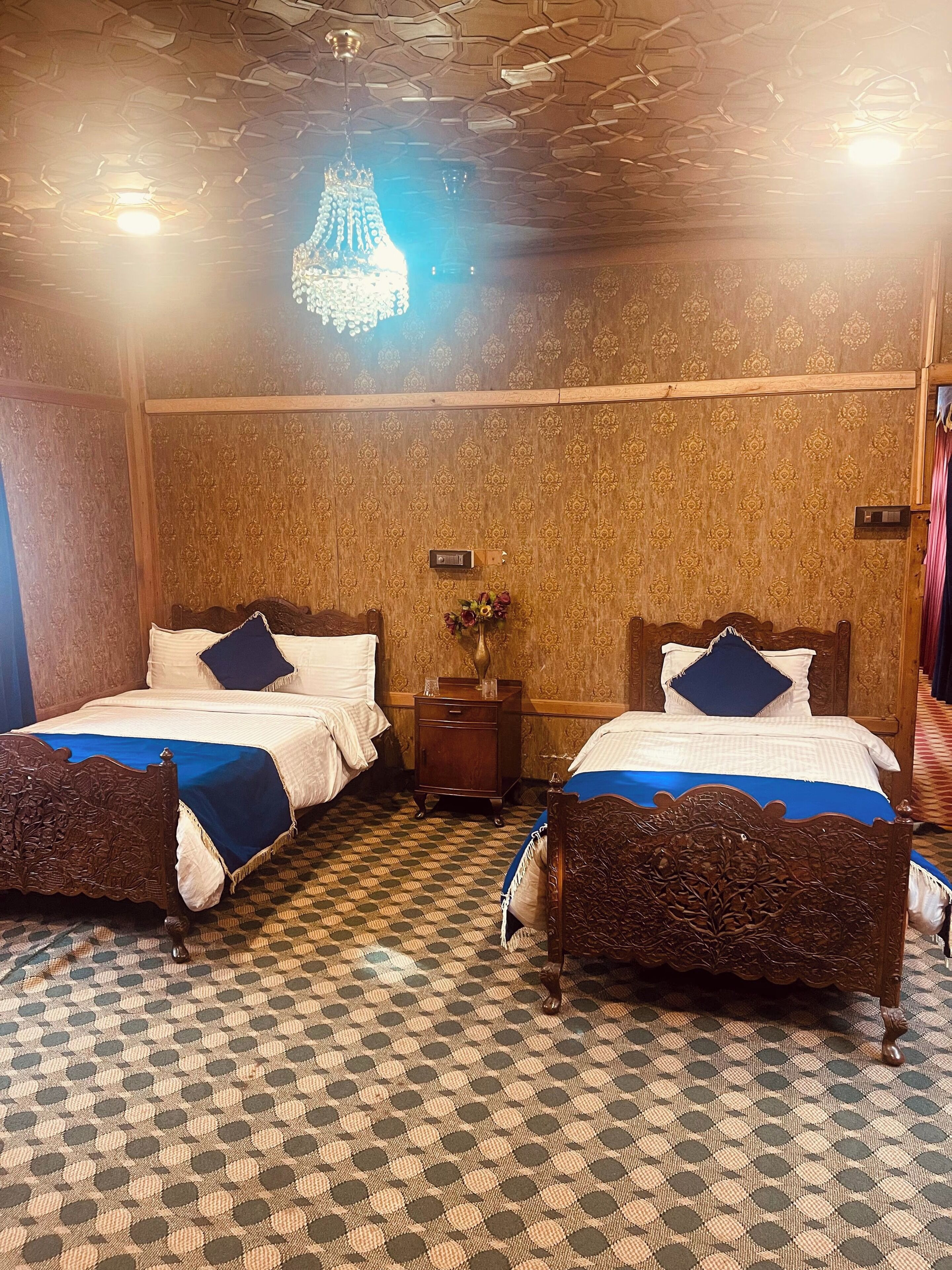 A hotel room with two beds, a patterned floor, and a chandelier.