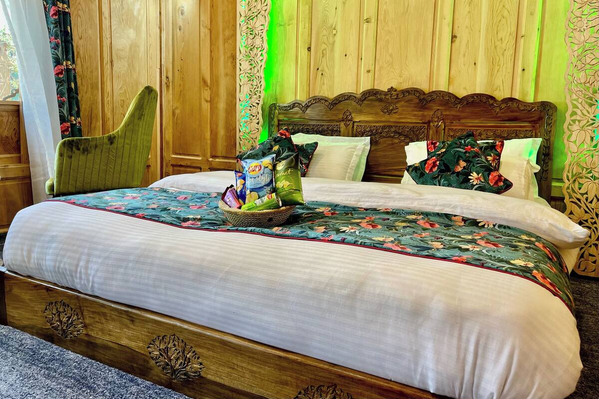 A wooden bed with floral bedding, a green chair, and a basket of snacks.