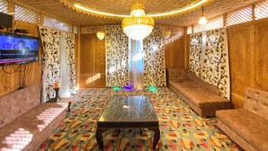 A room with a patterned carpet, a glass-top table, sofas, a television, and a chandelier. - The Apollo 11 Heritage Luxury Houseboat (Srinagar)