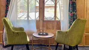 A room with two green upholstered chairs, a small round table with two wine glasses, and a window with floral curtains. - The Apollo 11 Heritage Luxury Houseboat (Srinagar)