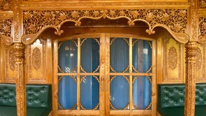 A richly carved wooden cabinet with glass panels and green upholstered seating. - The Apollo 11 Heritage Luxury Houseboat (Srinagar)