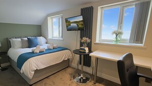 Ein Hotelzimmer mit Bett, Schreibtisch, Stuhl, Fernseher und einem Fenster mit Vorhängen.