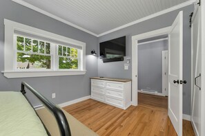 A bedroom with a bed, a dresser, a television, and a window with a view of trees. - Quaint Bethel Home with Firepit - Walk to Town (Bethel)