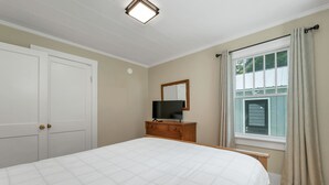 A bedroom with a bed, a dresser, a television, a window with curtains, and a door. - Quaint Bethel Home with Firepit - Walk to Town (Bethel)