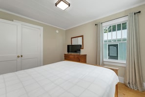 A bedroom with a bed, a dresser, a television, a window with curtains, and a door. - Quaint Bethel Home with Firepit - Walk to Town (Bethel)