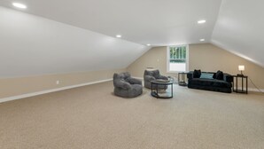 A spacious attic room with a sloped ceiling, a large window, and a cozy seating area with a sofa and two armchairs. - Quaint Bethel Home with Firepit - Walk to Town (Bethel)
