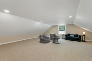 A spacious attic room with a sloped ceiling, a large window, and a cozy seating area with a sofa and two armchairs. - Quaint Bethel Home with Firepit - Walk to Town (Bethel)