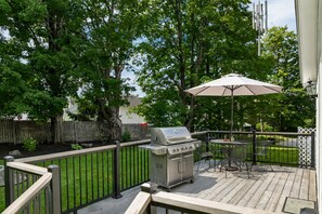 Une terrasse en bois avec un barbecue, du mobilier d’extérieur et une clôture.