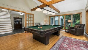 A pool table in a room with wooden beams, a bookshelf, and a view through large windows. - Quaint Bethel Home with Firepit - Walk to Town (Bethel)