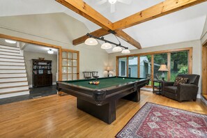 A pool table in a room with wooden beams, a bookshelf, and a view through large windows. - Quaint Bethel Home with Firepit - Walk to Town (Bethel)