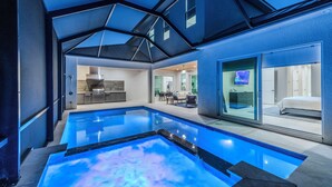 Een modern binnenzwembad met glazen dak, een keukenhoek en een slaapkamer met televisie.