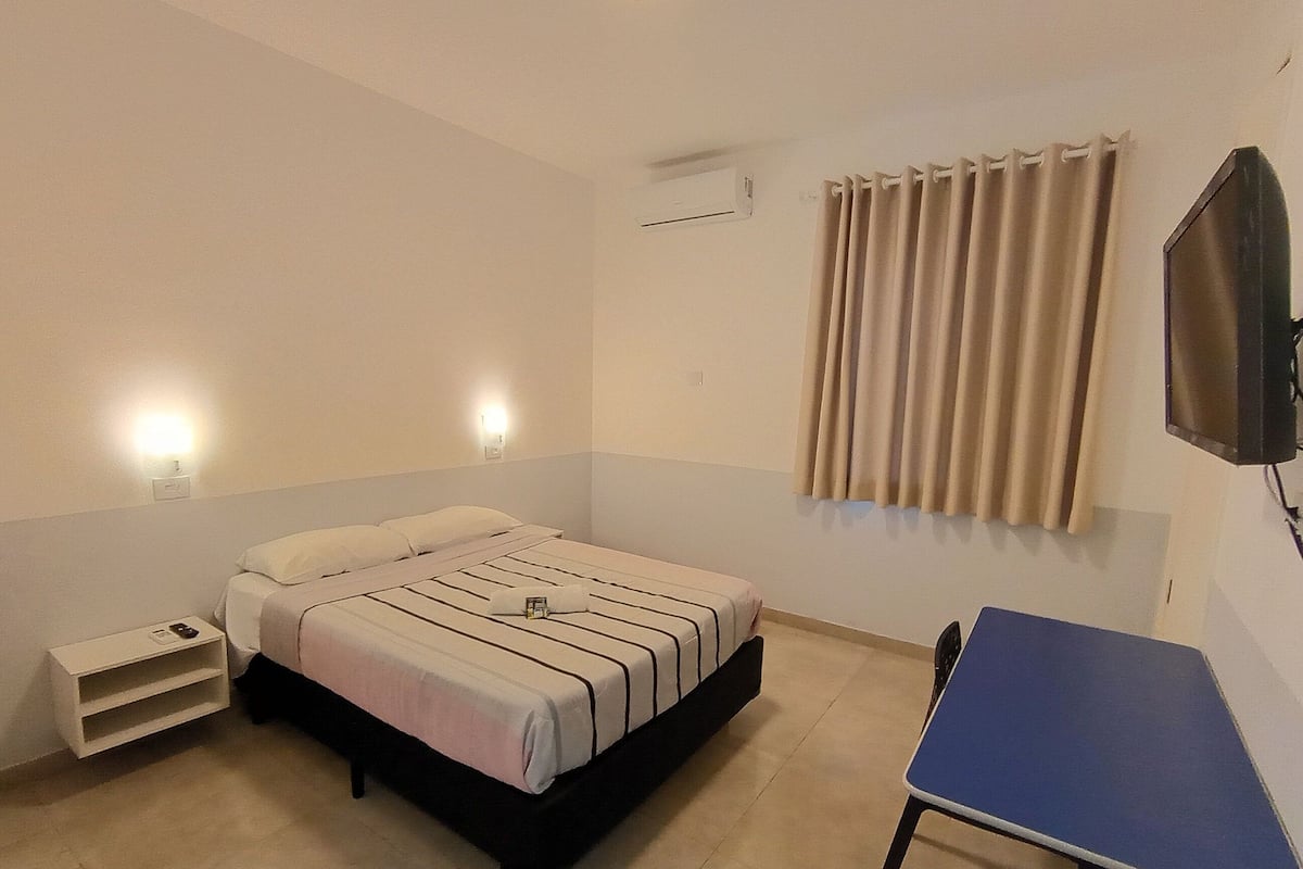 A hotel room with a bed, bedside tables, a desk, and a television.