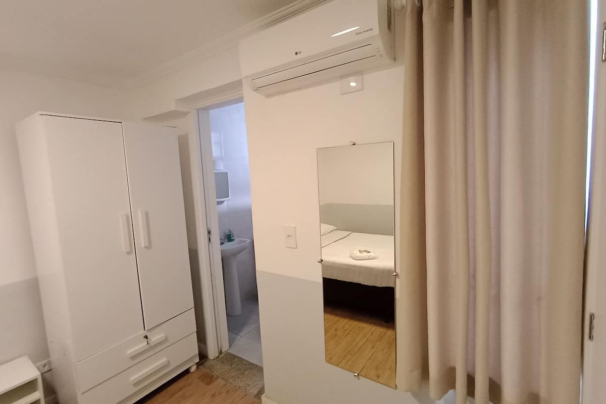 A room with a wardrobe, a mirror, a bedside table, and a bathroom visible through an open door.