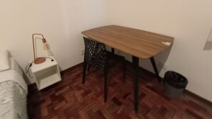A small room with a wooden table, a white nightstand, a black chair, a white sofa, and a trash bin. - WeStay Budget-Unidade 3 (São Paulo)