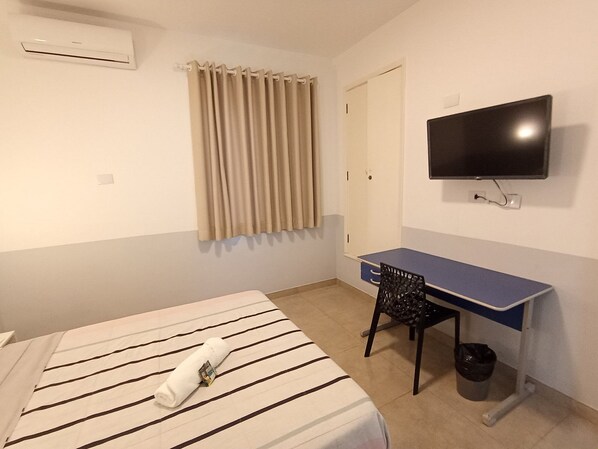 Une chambre d’hôtel équipée d’un lit, d’un bureau, d’une chaise, d’une télévision et d’une fenêtre avec des rideaux.