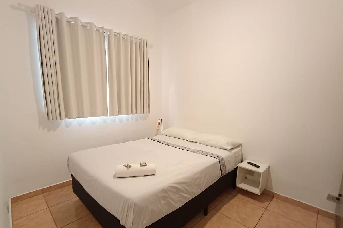 A single bed with a white mattress and a small bedside table with a lamp.