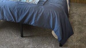Un dormitorio con cama, paredes de madera, una ventana con persianas y una lámpara colgante.