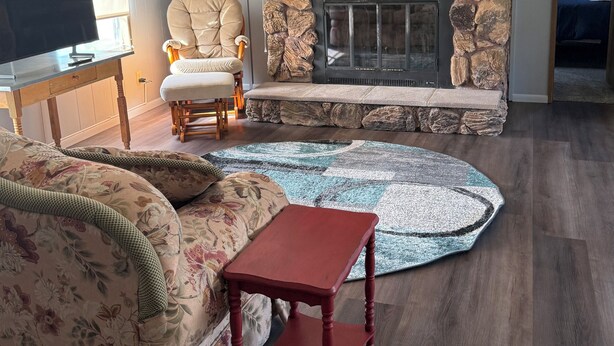 Una sala de estar con chimenea de piedra, televisor, sofá, sillón y una mesita.