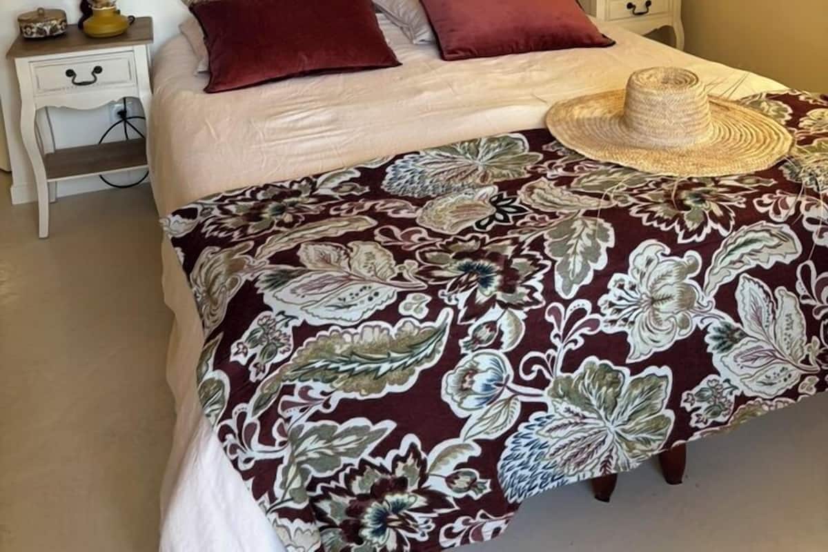 A bedroom with a bed, a nightstand, a decorative wall piece, and a view through a window.