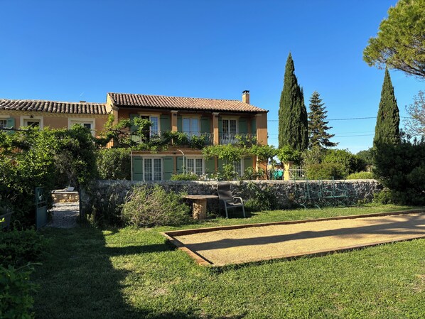 A villa with a garden, a tennis court, and a stone wall.