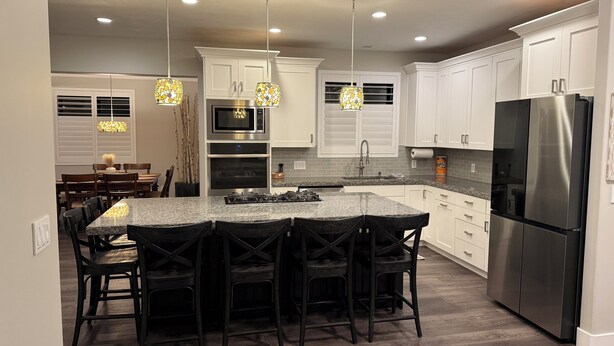 A modern kitchen with white cabinets, a stainless steel refrigerator, and a granite island with bar stools. - Utah Vista Chalet: Amazing View Deck, Dual Kitchens & Hot Tub, Games  Sleeps 15 (South Jordan)