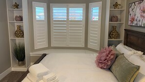 A bedroom with a large bed, white shutters, decorative vases, and a view of the outside. - Utah Vista Chalet: Amazing View Deck, Dual Kitchens & Hot Tub, Games  Sleeps 15 (South Jordan)