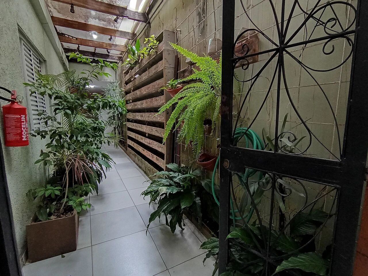 A narrow hallway with tiled flooring, potted plants, a wooden fence, and a metal gate.