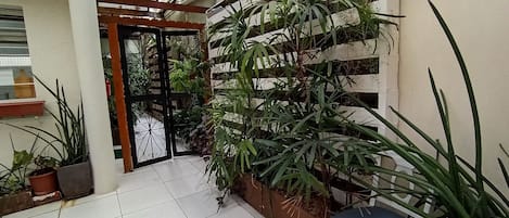 A covered patio area with tiled flooring, a wooden pergola, and various potted plants.