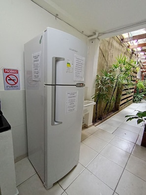 A white refrigerator with a freezer compartment, a 'Proibido Fumar' sign, and a 'Bebidas para Utilização da Geladeira' sign. - WeStay Budget - Unidade 4 (São Paulo)
