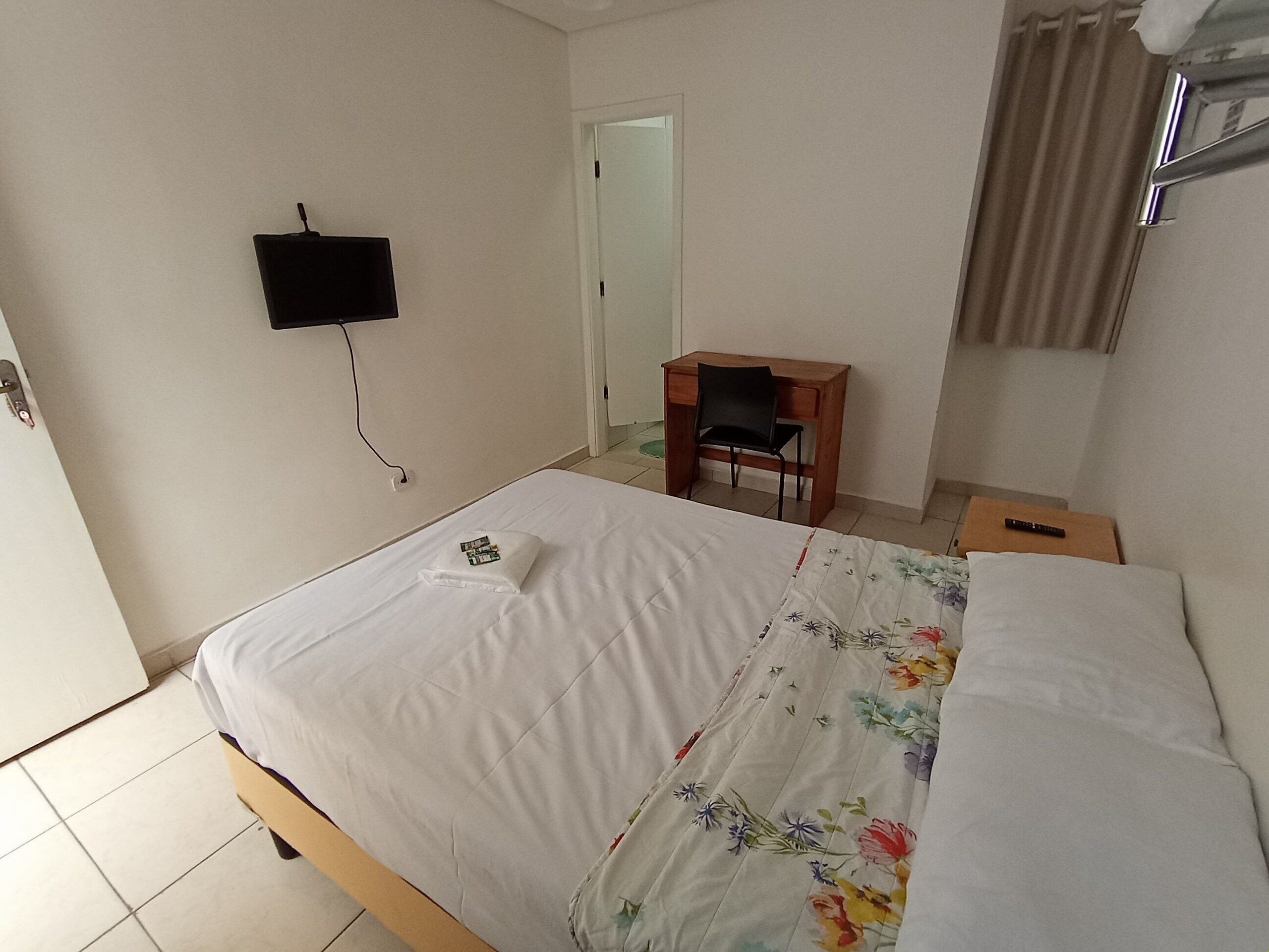 Une chambre d’hôtel équipée d’un lit, d’un bureau, d’une chaise et d’un téléviseur fixé au mur.