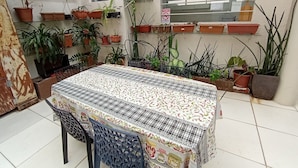 A dining area with a table covered in a patterned tablecloth, surrounded by chairs. There are multiple potted plants on shelves and hanging pots. - WeStay Budget - Unidade 4 (São Paulo)