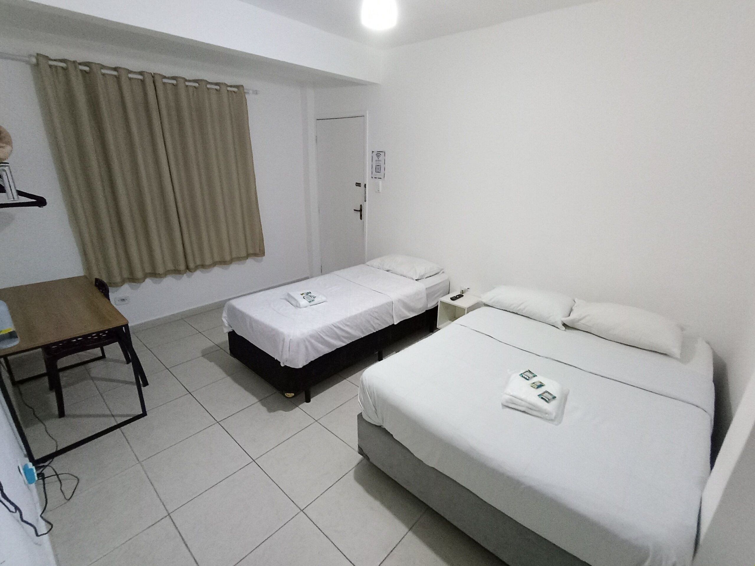 A small, clean room with two beds, a desk, and a window with curtains.