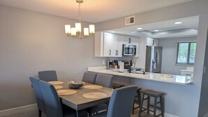Una cocina moderna con armarios blancos, electrodomésticos de acero inoxidable y una isla central con taburetes de bar.