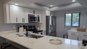Una cocina moderna con armarios blancos, electrodomésticos de acero inoxidable, encimera de mármol y taburetes de bar.