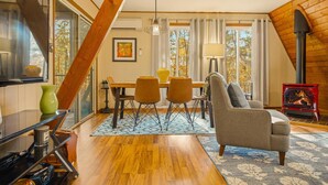 Uma sala de estar aconchegante com lareira, uma área de jantar com mesa e cadeiras, e uma janela grande com cortinas.