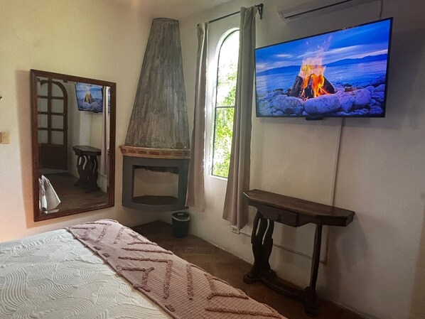 A bedroom with a bed, a television displaying a fire scene, a mirror, and a window with curtains. - Casa Loreto 29 San Miguel de Allende (San Miguel de Allende)