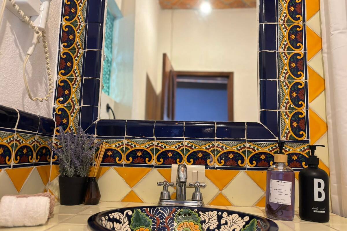 Une salle de bain avec un mur recouvert de carreaux décoratifs, un lavabo orné d’un motif floral, un miroir, une serviette et des articles de toilette.
