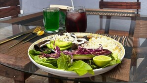 Una mesa de comedor con un plato de ensalada, dos bebidas y cubiertos. Un letrero arriba dice "SANTORIA RESTAURANTE".