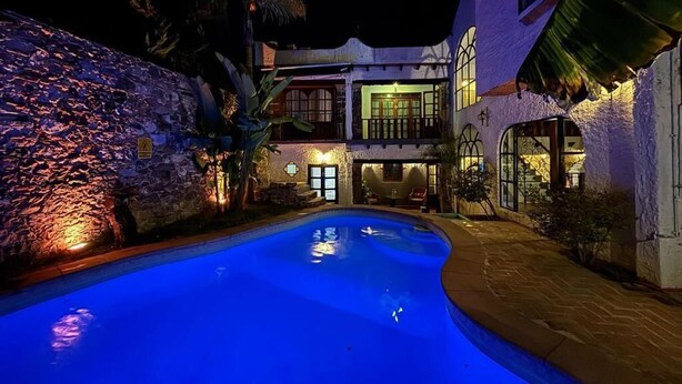 Vista nocturna de un área de piscina con un muro de piedra y un edificio de dos plantas con balcones.