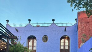 Un edificio con fachada azul, ventanas arqueadas y un sendero de ladrillo que conduce a la entrada.