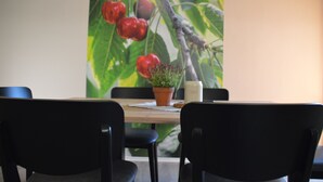 Mesa de jantar com uma planta em vaso e uma vela, diante de uma parede com painel de árvore frutífera.