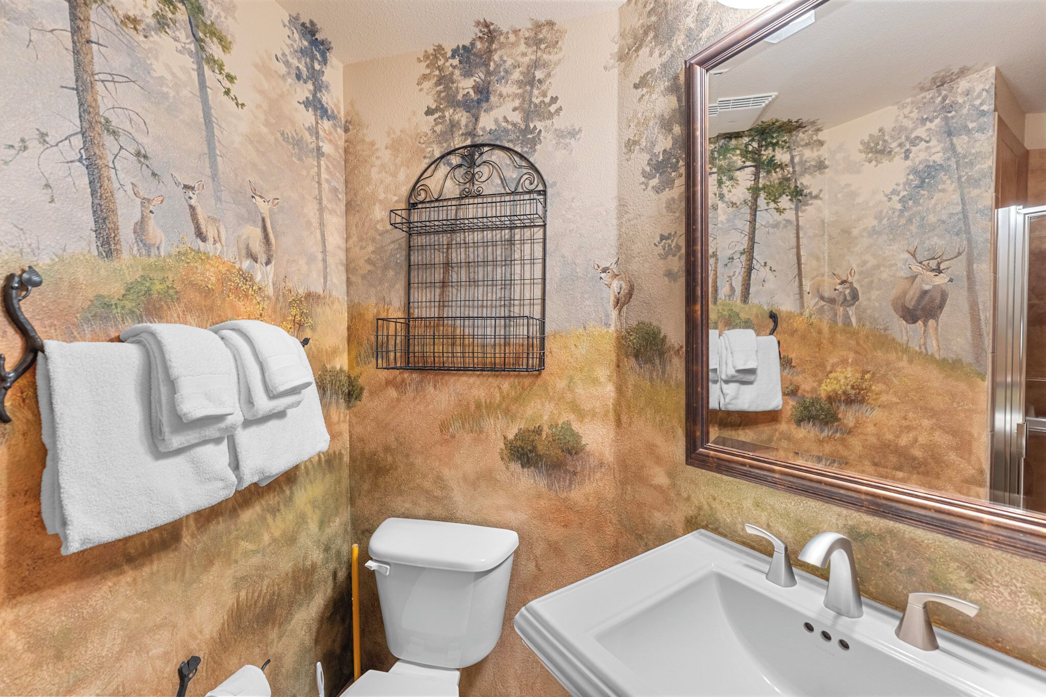 A bathroom with a deer mural, a hanging toilet paper holder, and a sink with a mirror.