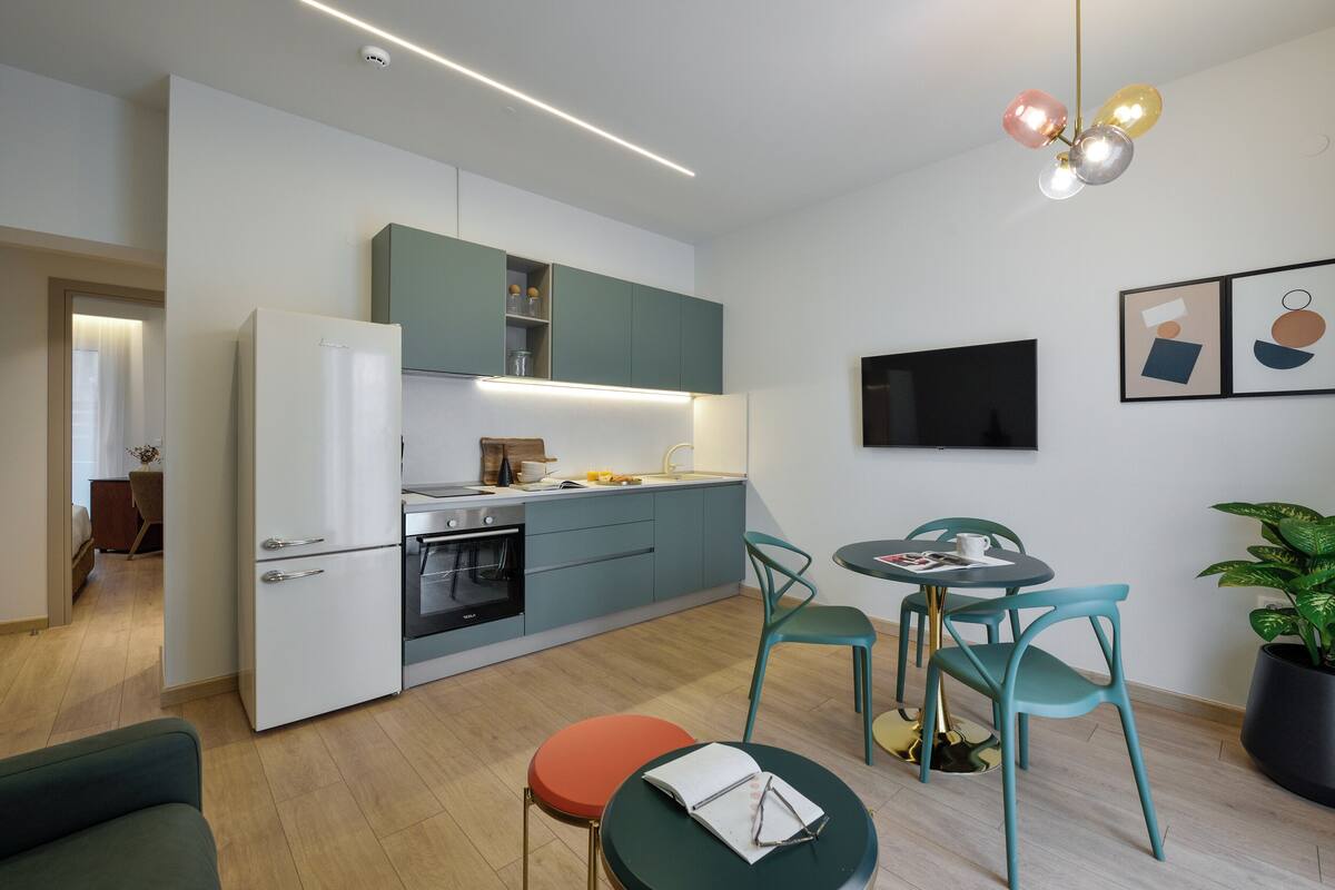 Una cocina moderna con horno empotrado, una zona de comedor con una mesita y sillas, y una planta en maceta.
