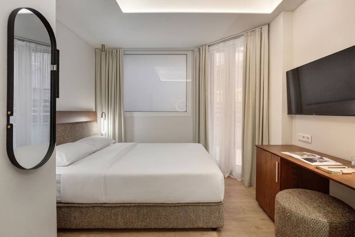 Una habitación de hotel con cama, escritorio, televisor y ventana con cortinas.