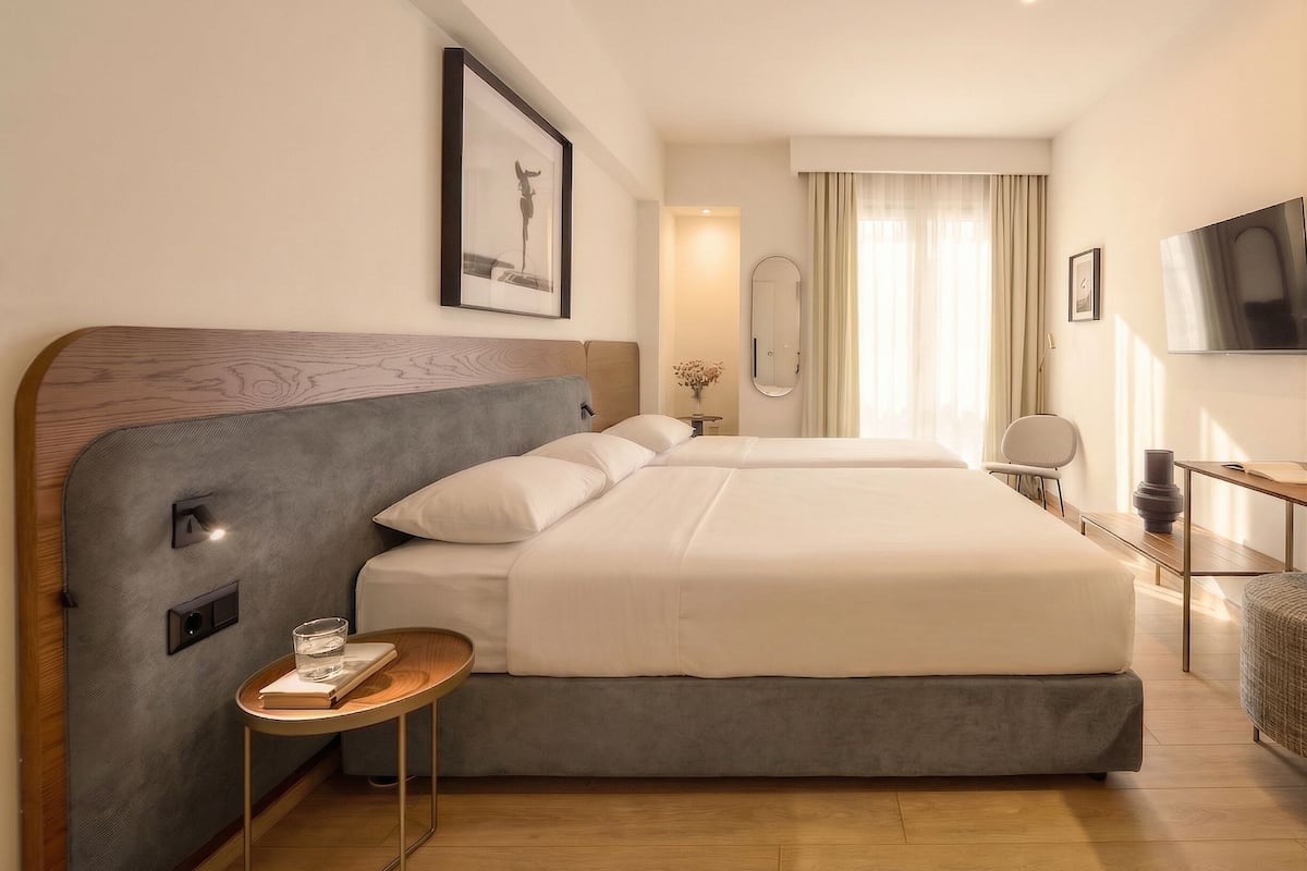 Una habitación de hotel con una cama grande, mesitas de noche, un televisor y un espejo.